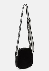 Črna najlon torba za čez ramo v pravokotnem obliku, z bleščečo teksturo in nastavljivim pasom, na katerem je odtisnjen napis "KARL LAGERFELD JEANS".