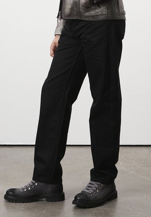 Zwarte rechte broek van duurzaam materiaal, met een eenvoudig ontwerp, gecombineerd met robuuste grijze wandelschoenen met veters.