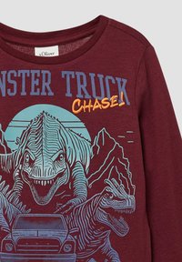 Bordeauxfarbenes Langarmhemd mit einem Dinosaurier- und Monstertruck-Motiv. Der Text lautet "MONSTER TRUCK CHASE!" in blauer und orangener Schrift.