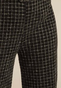 Pantalon à carreaux noir et blanc avec un tissu texturé, présentant un motif en grille et une coupe ajustée. Coutures visibles et détails de poches.