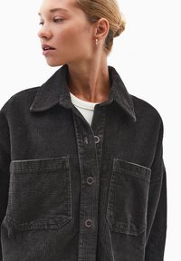 Sort fløjlsjakke med knaplukning, to store forlommer og en klassisk krave. Har en lodret ribbet struktur.