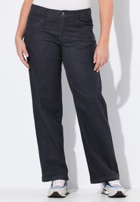 Donker denimjeans met een recht model, vijf zakken en een knoopsluiting, gecombineerd met meerkleurige sportschoenen.