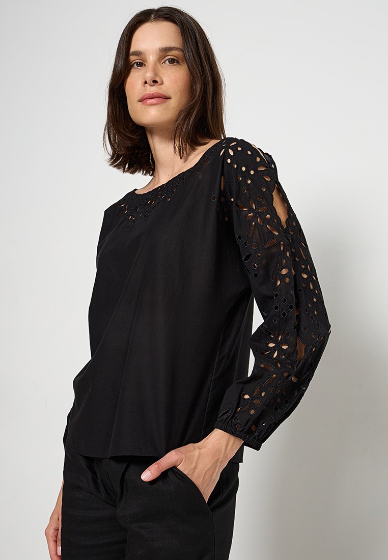 Czarna bluzka z haftowanymi wycięciami na rękawach i dekolcie, o luźnym kroju i gładkiej fakturze.