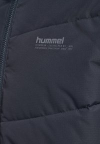 Svart puffjacka med texturerad tyg, med dragkedja och en logotyp präglad på bröstet. Kompakt och lätt design.