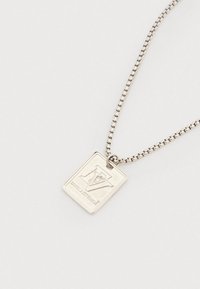 Ezüst téglalap alakú medál nyaklánc, amelyen a "FV" gravírozva van a "FAVELASTUDIOS" fölött, láncon, fehér háttér előtt.