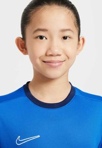 Camisa atlética azul con un cuello redondo en navy, con un logo de Nike blanco en el pecho. Textura suave, mangas cortas y corte ajustado.