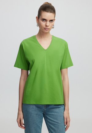 T-shirt verde a V in cotone morbido con maniche corte e vestibilità rilassata, abbinato a jeans in denim blu chiaro.