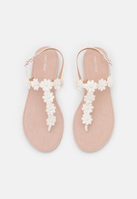 Flat sandals with a nude faux suede insole, featuring white floral embellishments and adjustable ankle straps.