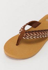 Brown flip-flop featuring a braided strap in brown and cream colors, a flat tan footbed with a subtle texture, and a rounded toe design.