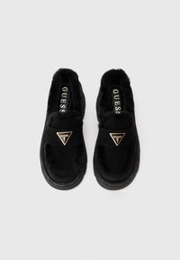 Sorte slip-on sko med blødt pelsfor, overdel i ruskind og et guld trekantet logo på stropen; tekstureret gummisål.