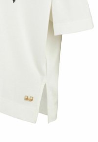 White cotton t-shirt featuring short sleeves, side slits, and a gold-tone logo accent near the hem. Smooth texture, casual design.