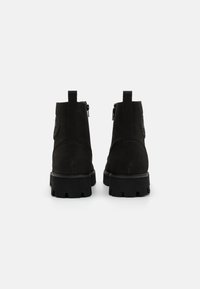 Bottines noires à talon avec une texture en daim, fermeture éclair à l'arrière et semelle épaisse. Design minimaliste avec une languette au talon et sans ornements.