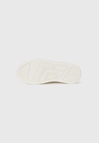 Semelle de basket blanche avec des motifs de grip texturés, présentant un design à motifs et un bout arrondi, sur un fond uni.