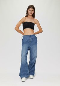 Lichte blauwe denim broek met wijde pijpen en een drawstring taille. Gecombineerd met een zwarte strapless top. Zachte textuur, casual pasvorm en minimale details.