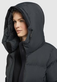 Veste doudoune en gris foncé, dotée d'une grande capuche, d'une fermeture éclair et d'une texture douce. Comprend un matériel ajustable pour un ajustement sécurisé.