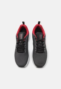 Scarpe sportive nere con una tomaia in mesh testurizzato, accenti rossi sulla parte superiore, lacci neri e suole bianche con un design uniforme.