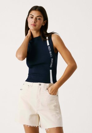 Top senza maniche blu navy con testo "RED BULL RACING" bianco lungo il lato. Abbinato a pantaloni corti di colore chiaro con orlo sfrangiato.