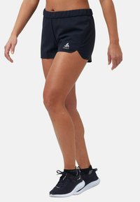 Mustat urheilusortsit, joissa on joustava vyötärö, sivuhalkiot ja pieni logo. Yhdistetty mustien juoksukenkiin, joissa on valkoiset pohjat.