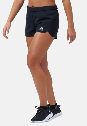 Schwarze Sportshorts mit einem elastischen Bund, seitlichen Schlitzen und einem kleinen Logo. Kombiniert mit schwarzen Laufschuhen mit weißen Sohlen.
