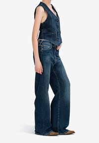 Džínová vesta s vypasovaným střihem a pěti knoflíky, kombinovaná s širokými džínovými kalhotami v tmavomodrém praní. Texturovaná látka po celém povrchu.