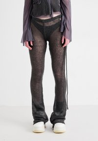 Svarte strikkede bukser med et gjennomsiktig, teksturert design og vide ben, kombinert med en kort, semi-transparent topp og hvite sneakers.