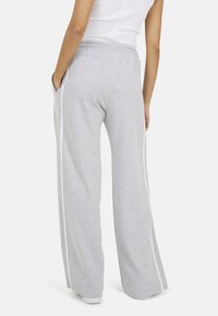 Grijze sweatpants met een losse pasvorm, gemaakt van zachte stof. Heeft witte zijkantenstrepen en een elastische tailleband, met zichtbare zijzakken.