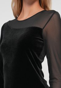 Black velvet top featuring sheer black mesh sleeves and a round neckline, highlighting a smooth texture and fitted design.