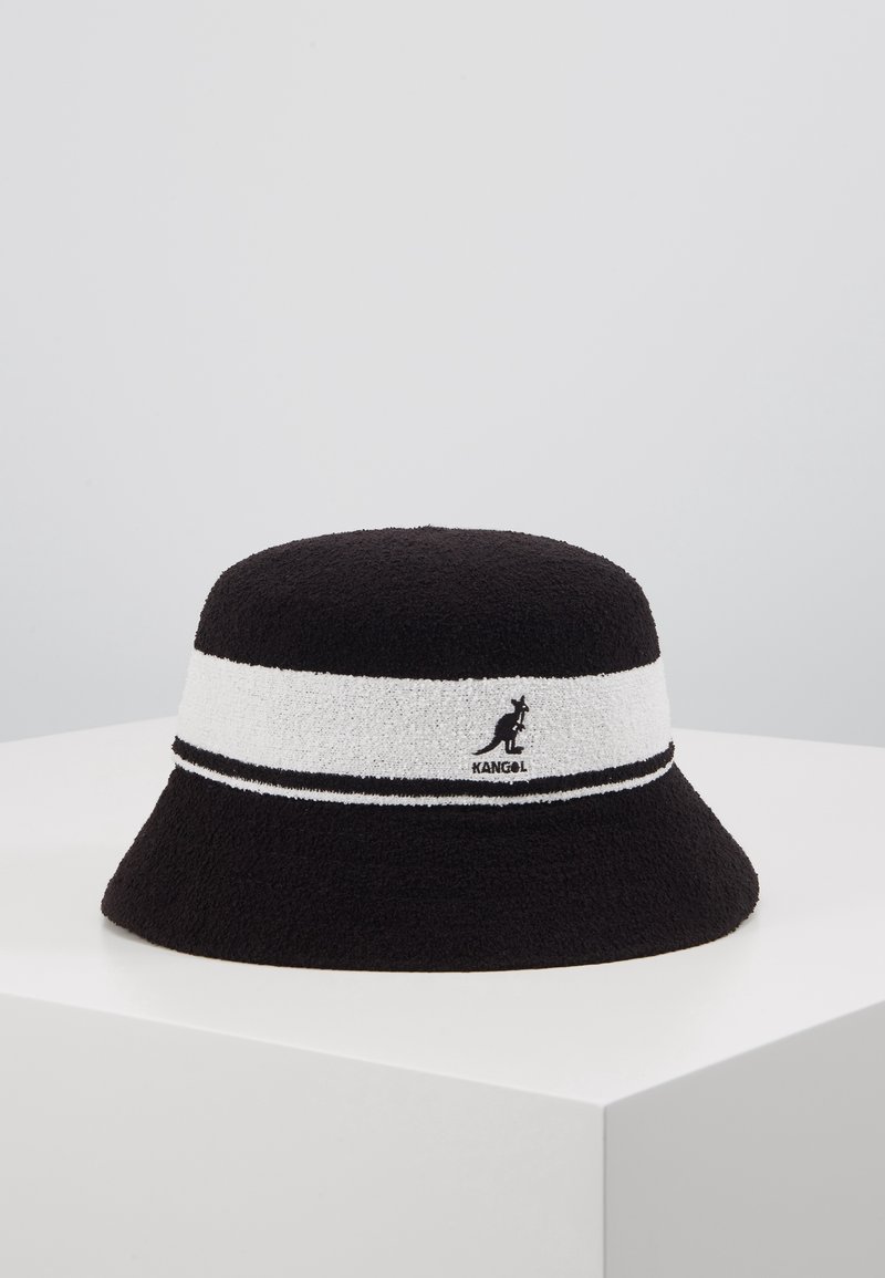 Chapeau seau noir avec bande blanche ornée du logo kangourou et du texte "Kangol", présenté sur un socle blanc sur un fond uni.