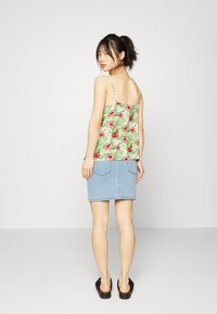 Top verde com estampado floral e alças finas, combinado com uma saia de ganga azul clara. O visual apresenta um corte solto e dois bolsos traseiros.