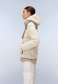 Chaqueta de forro polar en color crema, con un acabado texturizado, capucha y acentos en beige. Incluye bolsillos frontales y cremalleras para el cierre.