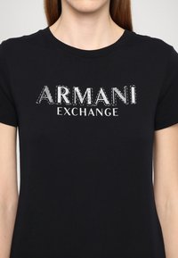 Svart bomull T-skjorte med en stor, metallisk sølv "ARMANI EXCHANGE" logo over brystet, med klassisk rund hals og korte ermer.