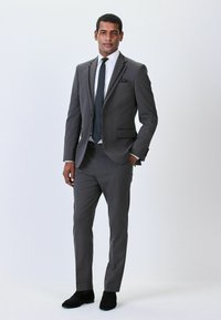 Costum gri cu design slim fit, cămașă albă, cravată neagră și batistă de buzunar. Pantofii din suede negru completează aspectul formal.