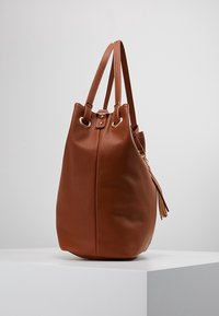 Brun læder bucket taske med tekstureret overflade, guldfarvet hardware, kvastdetalje og to skulderremme. Rund base med blød, slasket design.