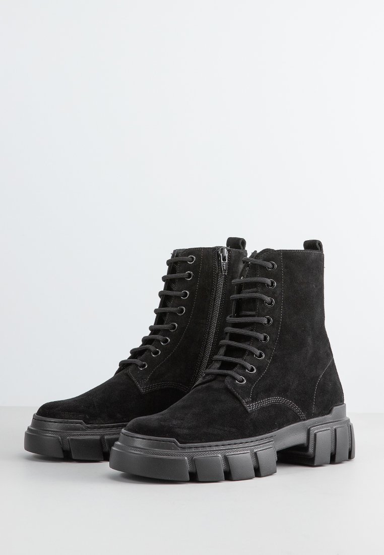 Botines de ante negros con cierres. Parte delantera con cordones y cremallera lateral, suela de goma resistente y detalles de costura en contraste.