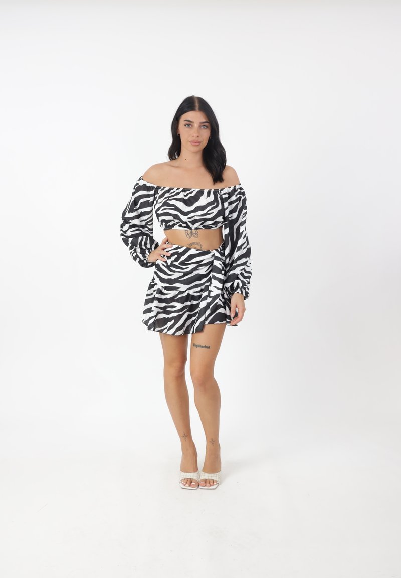 Top corto a stampa zebra bianco e nero con design scollato, abbinato a una gonna avvolgente coordinata. Tessuto morbido e vestibilità rilassata.
