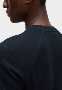 Tmavě modrý pletený svetr s kulatým výstřihem, texturovaným prošíváním podél ramenních švů a měkkým, hladkým povrchem.