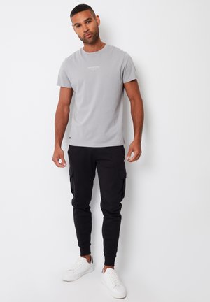 T-shirt grigio chiaro a maniche corte con testo stampato; abbinata a pantaloni cargo neri con tasche laterali; sneakers bianche.