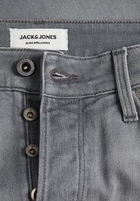 Jean de mezclilla gris con cierre de botones, botones de metal y una etiqueta que dice 'JACK & JONES JEANS INTELLIGENCE' en la cintura.