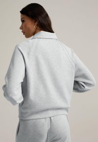 Grå fleecetröja med krage, som har en avslappnad passform och synliga sömmar. Mjuk textur, avslappnad design och långa ärmar.