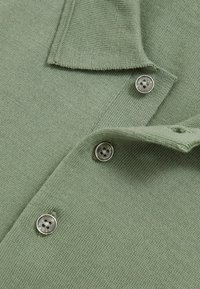 Hellgrünes Poloshirt aus strukturiertem Material, mit einem Kragen und drei metallischen Knöpfen am Knopfbereich.
