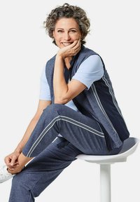 Sportliches Outfit mit einem hellblauen kurzärmligen Hemd und einer dunkelblauen Zip-Weste. Passende dunkelblaue Hose mit weißen Seitenstreifen.