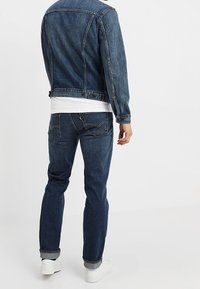 Denimjacka i mörkblått, med ribbade cuffar och krage. Kombinerad med mörkblå jeans och vita sneakers. Baksidan visar en rak passform.