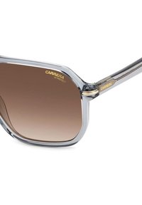 Occhiali da sole con tonalità marroni, montatura in plastica trasparente e dettagli in metallo. Logo "CARRERA UV PROTECT" visibile sull'obiettivo e sulla montatura.