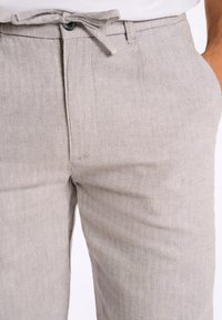 Pantalons en chevron gris clair avec taille nouée, fermeture à bouton et texture lisse. Dotés de poches latérales angulaires.