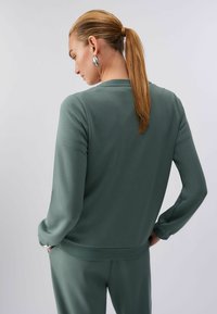 Sweat-shirt vert à texture lisse, col rond et manches longues. Présente une coupe décontractée et un ourlet côtelé. Vue de dos montrée.