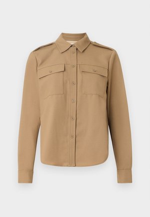 Chemise à manches longues en tissu beige avec un devant à boutons, deux poches poitrine, épaulettes et un ourlet incurvé.