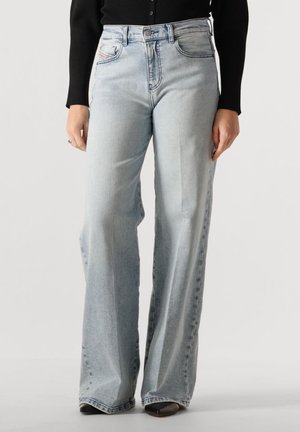 Jeans azzurri chiari a vita alta e gamba larga indossati con un top nero a maniche lunghe, mostrano la parte anteriore e parzialmente le gambe dalla vita ai piedi.