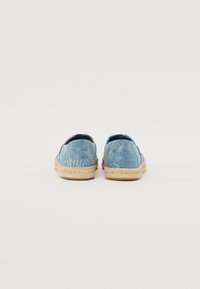 Scarpe in tessuto blu chiaro con un motivo a foglia impresso, suola in corda di juta e fodera in tessuto morbido. Design slip-on senza hardware visibile.