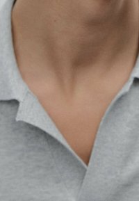 Szara koszulka polo z kołnierzykiem typu stójka, gładką fakturą i plisą na guziki. Zbliżenie na dekolt i obszar kołnierza.