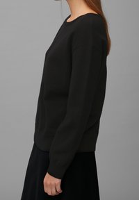 Schwarzer, langärmliger Pullover mit runden Ausschnitt, geripptem Saum und Bündchen. Weicher Stoff, kastiger Schnitt und minimalistisches Design.